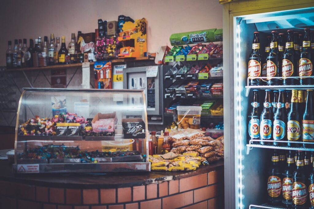 pexels-photo-64613 A well-stocked convenience store counter with snacks, drinks, and a refrigerator showcasing beverages.